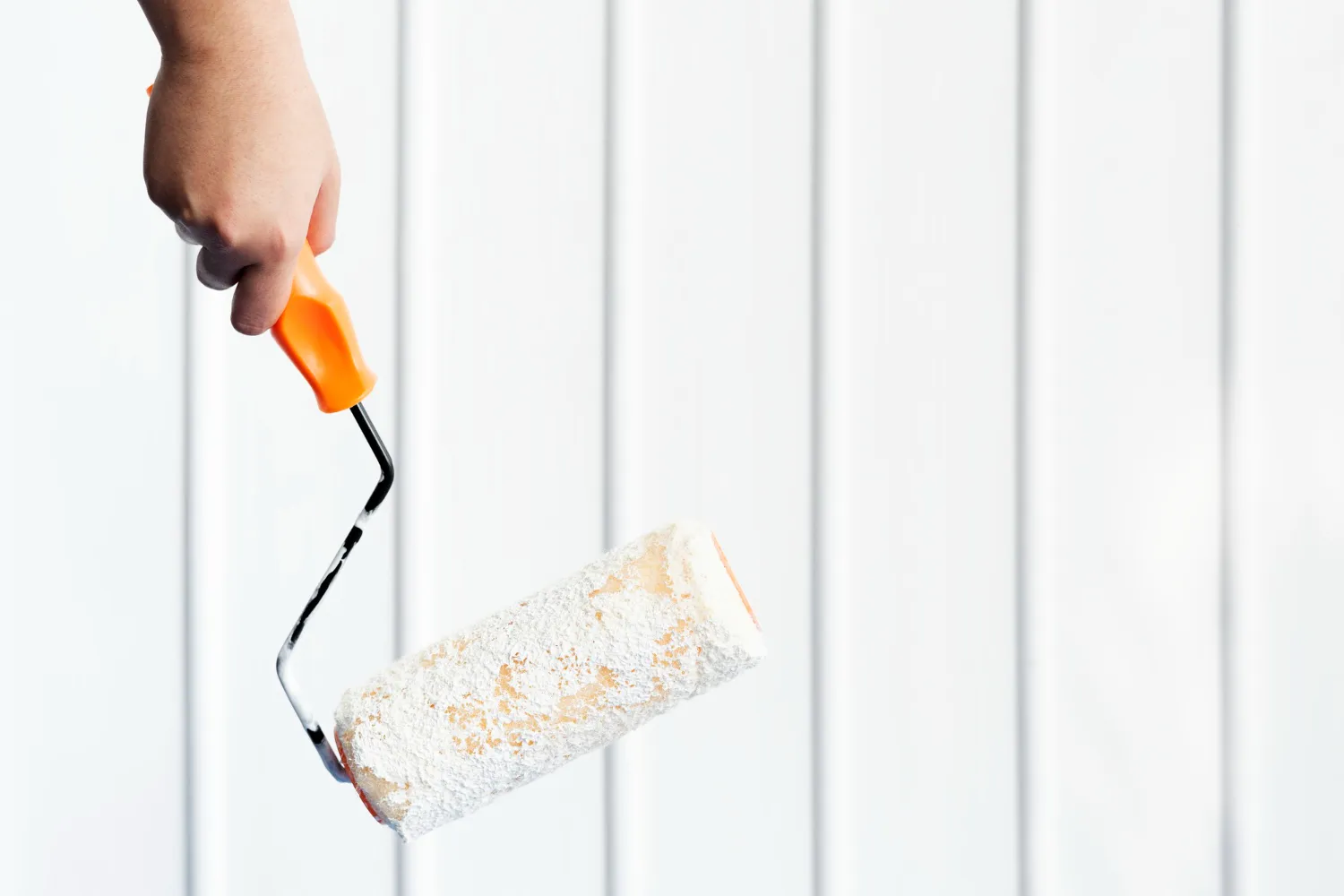 Rodillo de pintura sostenido por una mano, con un mango naranja, listo para aplicar pintura sobre una superficie blanca. Ideal para proyectos de renovación y decoración del hogar.