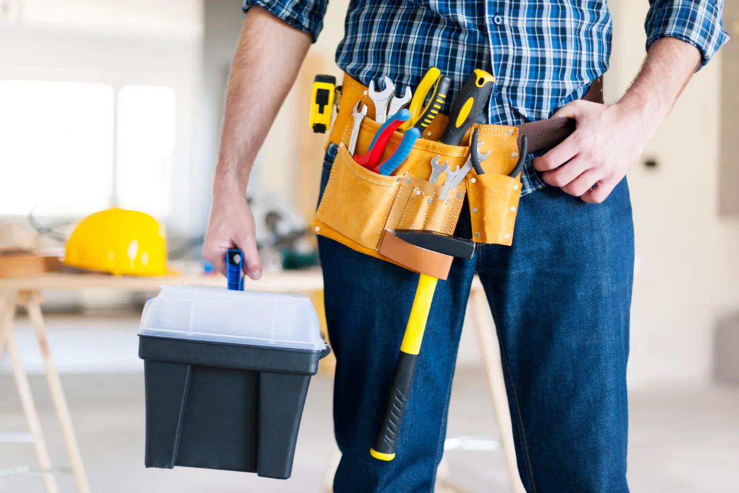 Hombre sosteniendo una caja de herramientas mientras usa un cinturón de herramientas lleno de diferentes utensilios en un entorno de construcción.